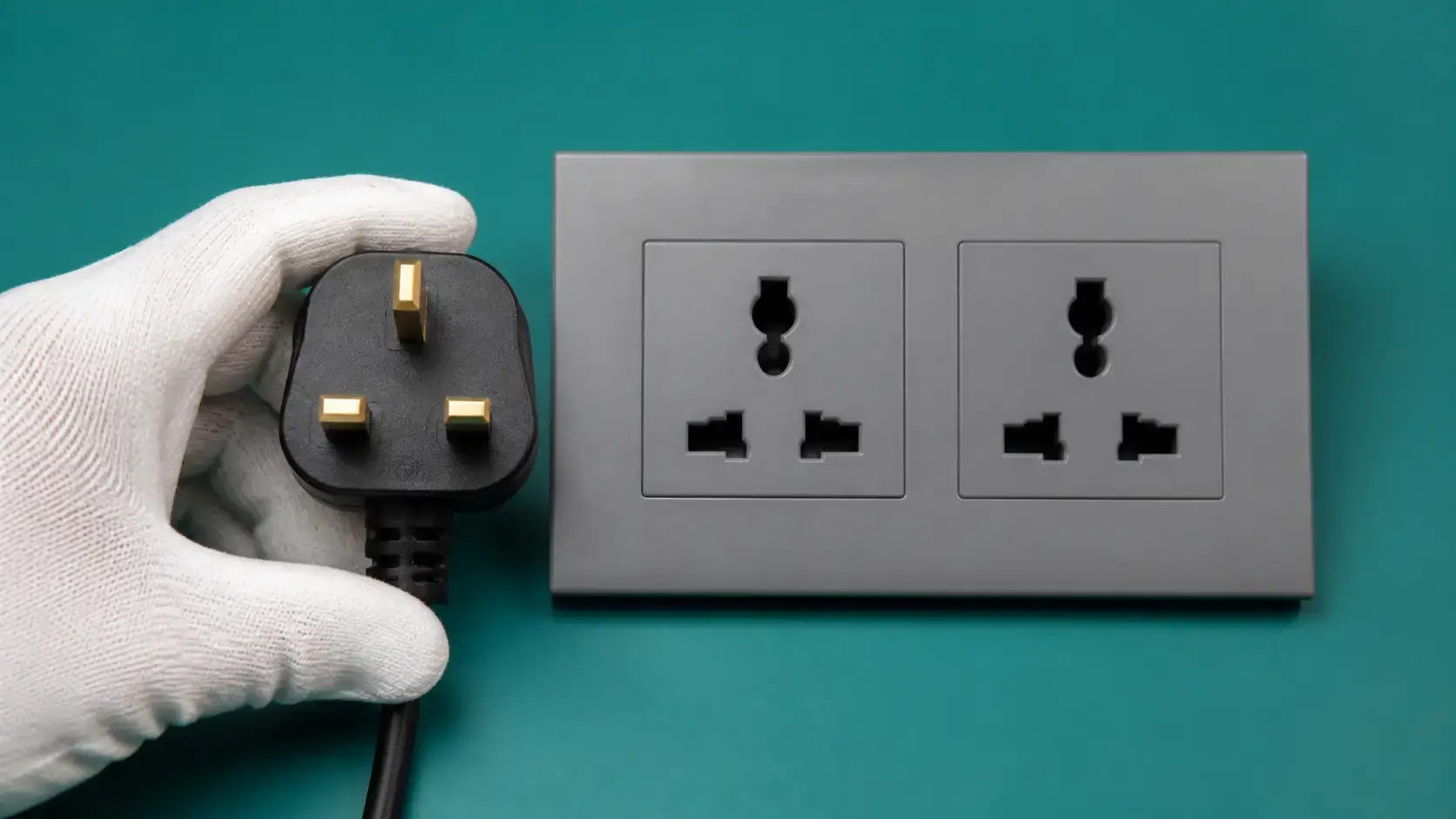 Three-pin UK plug aligned with a matt-grey two-gang universal wall socket for a de-energized fit check